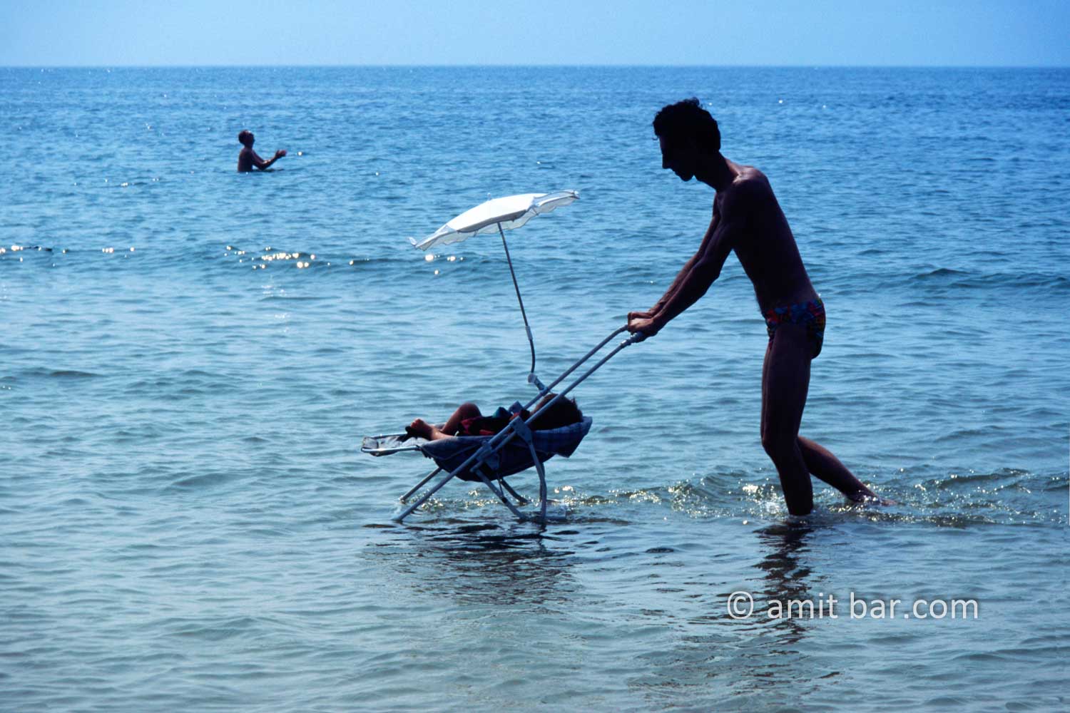 Cooling down: A man is pushing his baby-trolley in sea-water