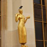 Three pigeons: A pigeon sits on golden sculpture with two pigeons